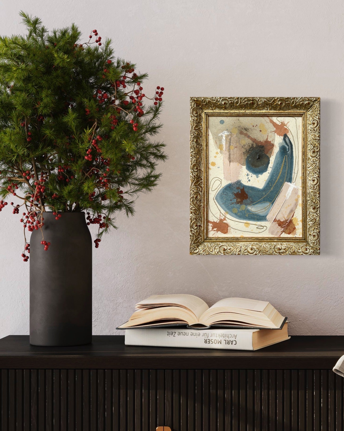 Decorative setup with a vase of greenery, open book, and framed artwork on a shelf.