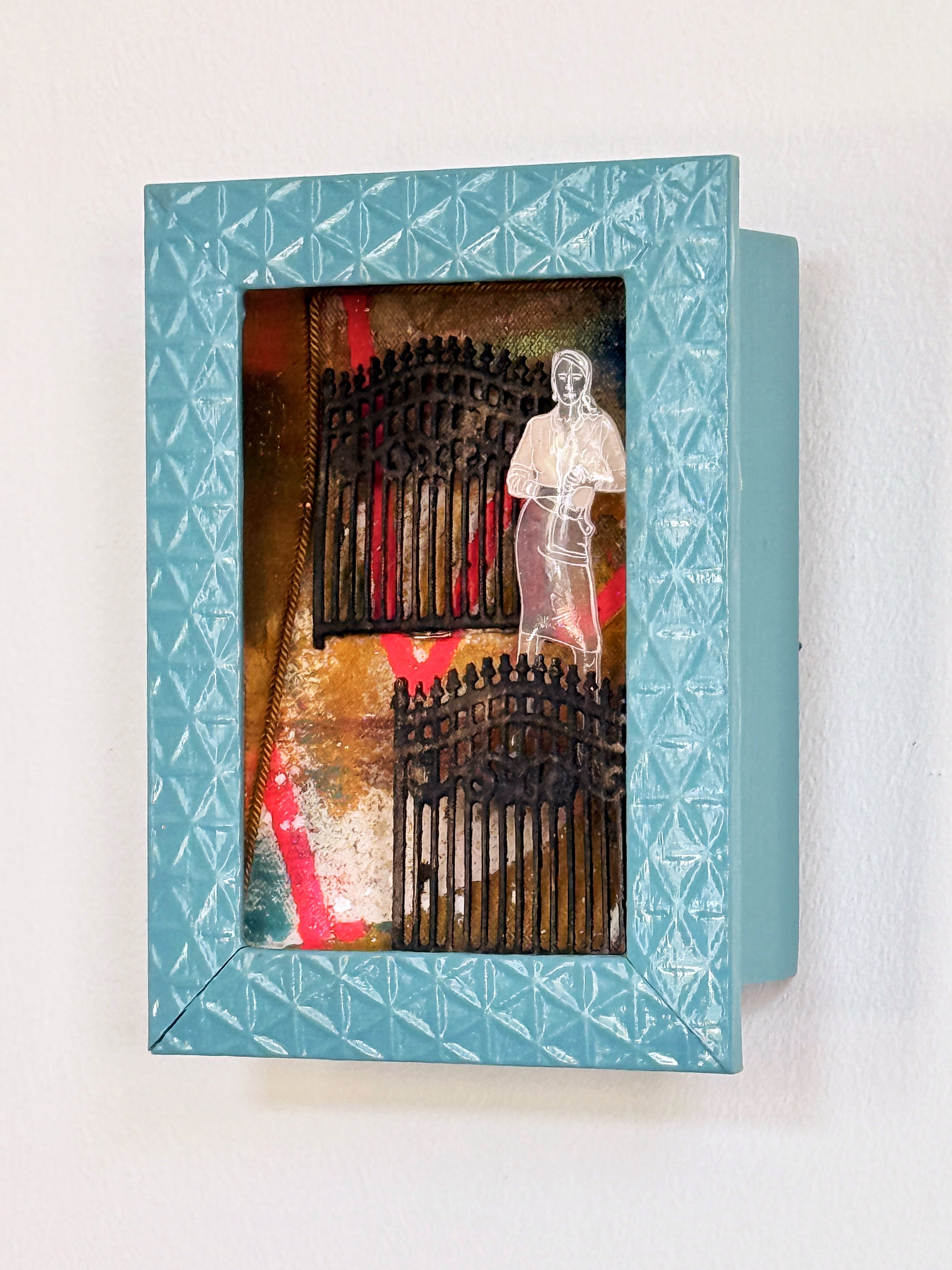 Decorative wall box with geometric patterned lid featuring a figurine and architectural elements.