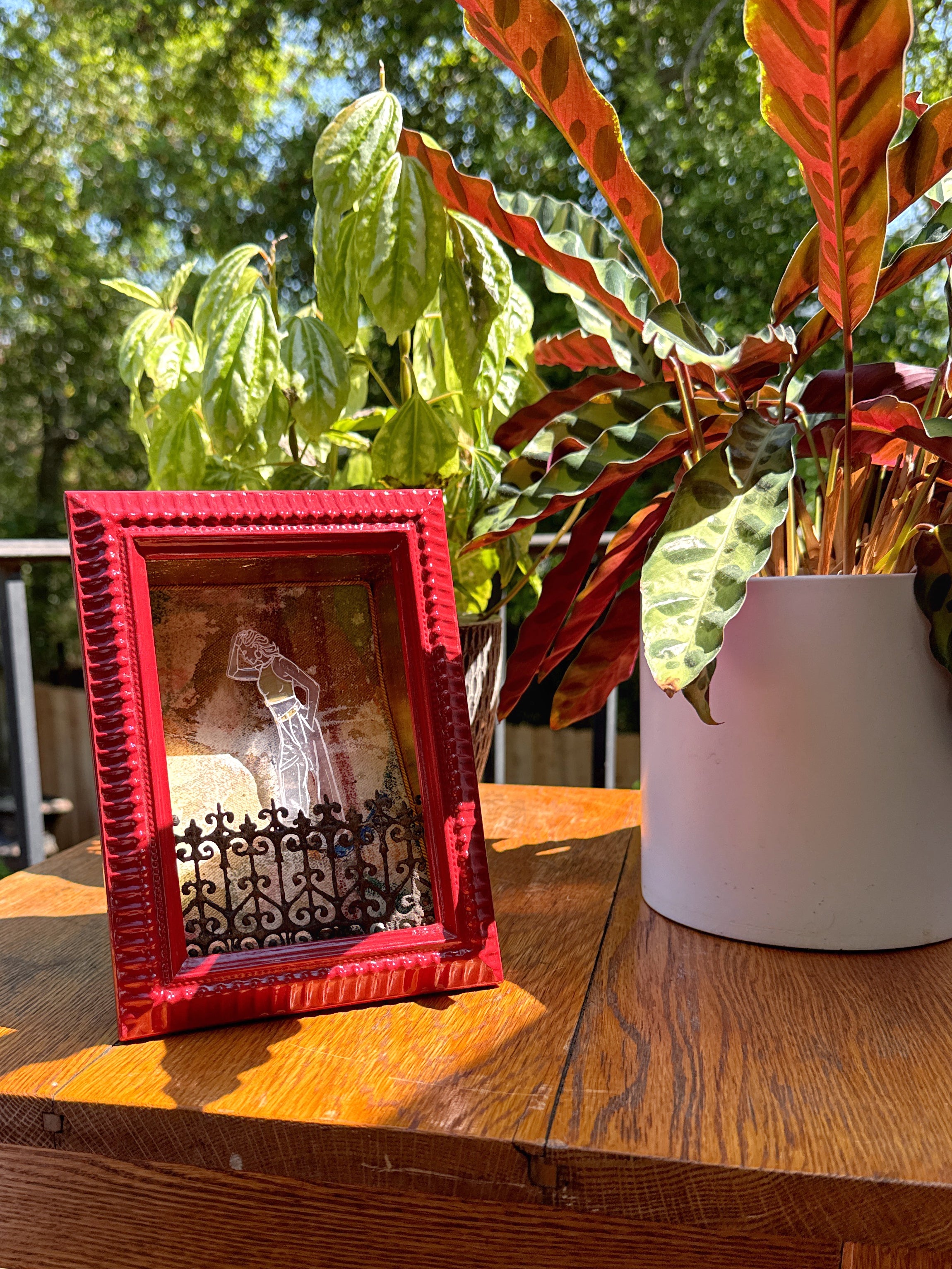 Red framed artwork on a wooden table with plants in the background