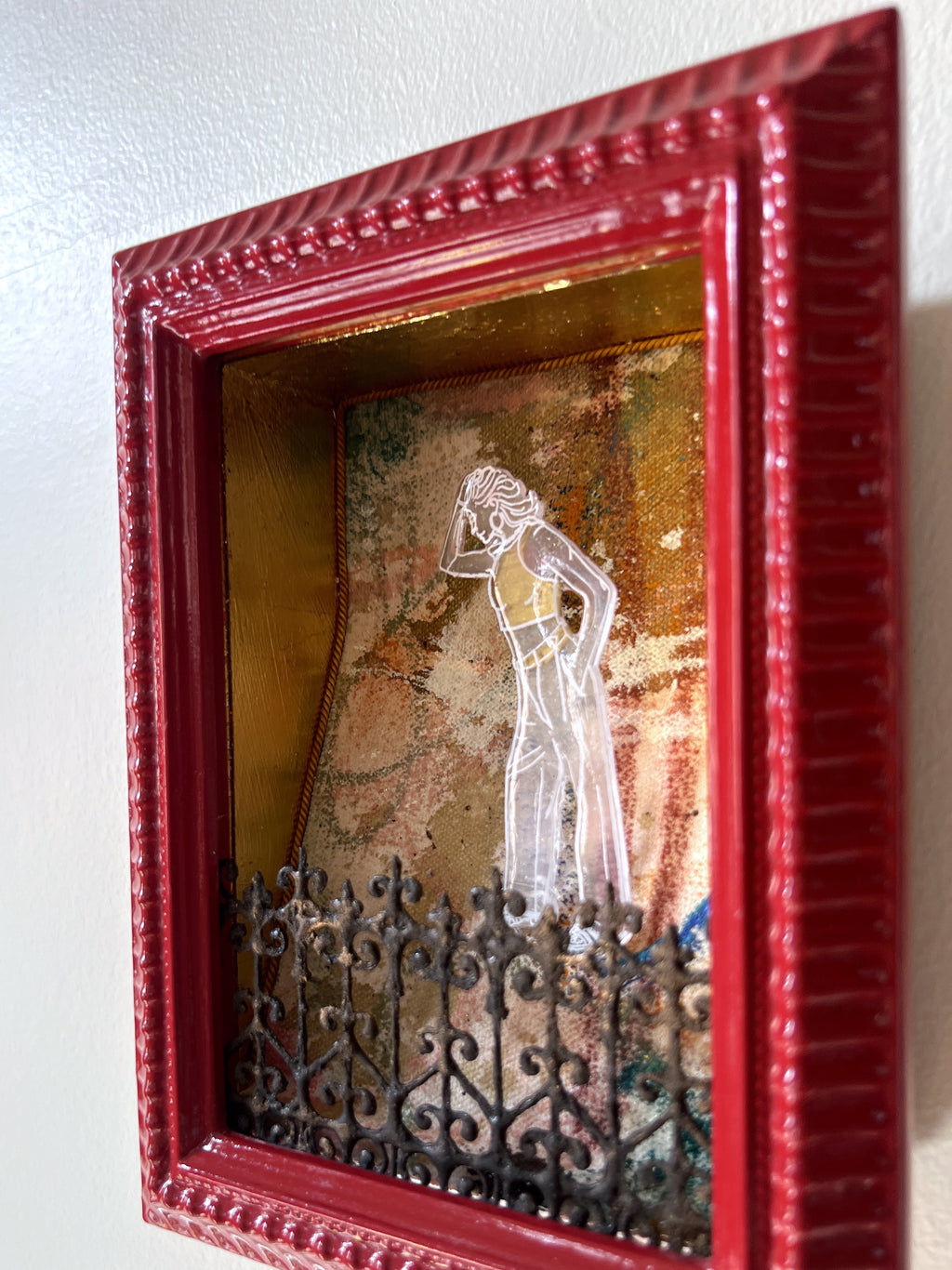 Decorative 3-dimensional wall art with a red frame featuring a silhouette of a woman and a fence.
