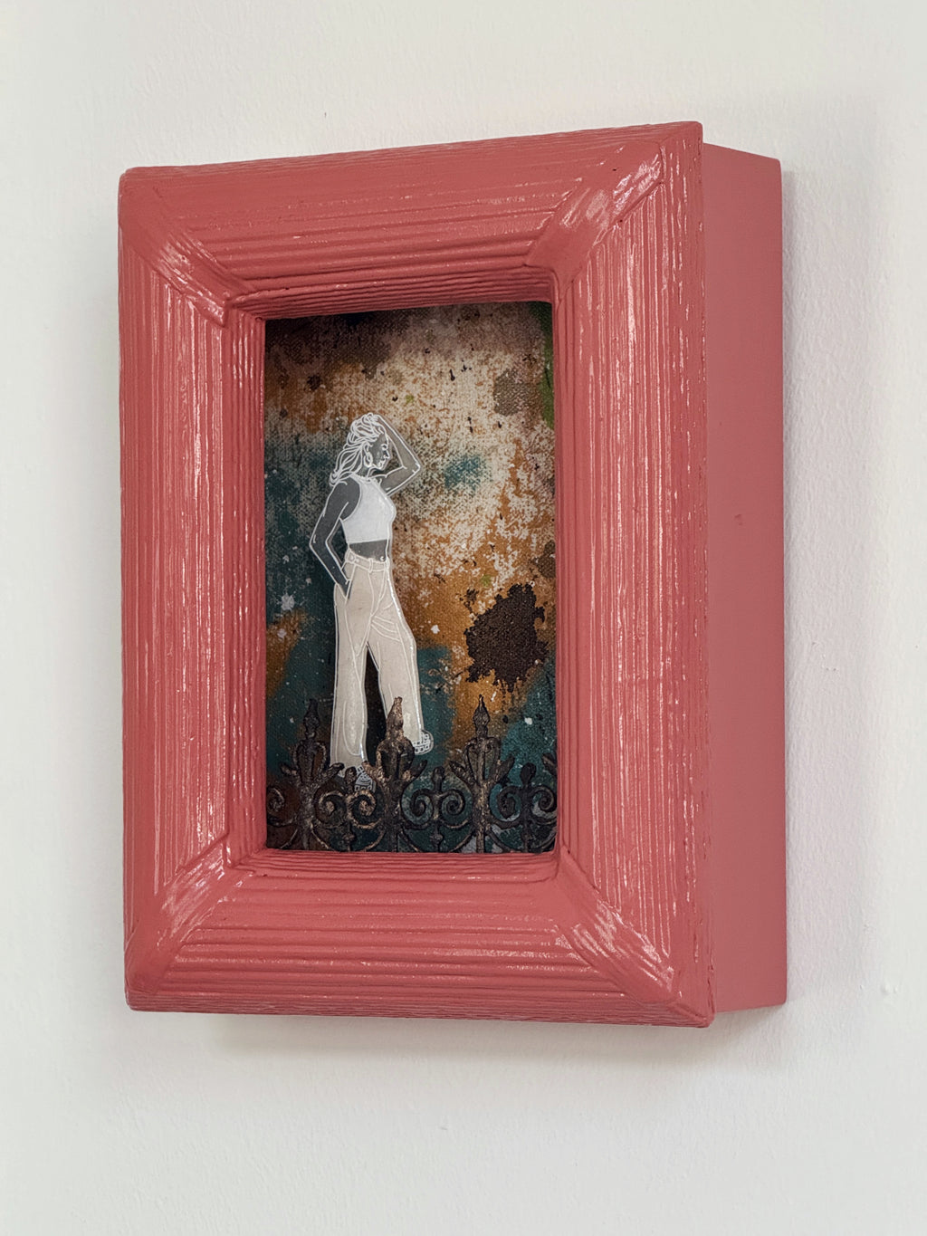 Small framed artwork with a woman's silhouette against a textured background, mounted on a white wall.