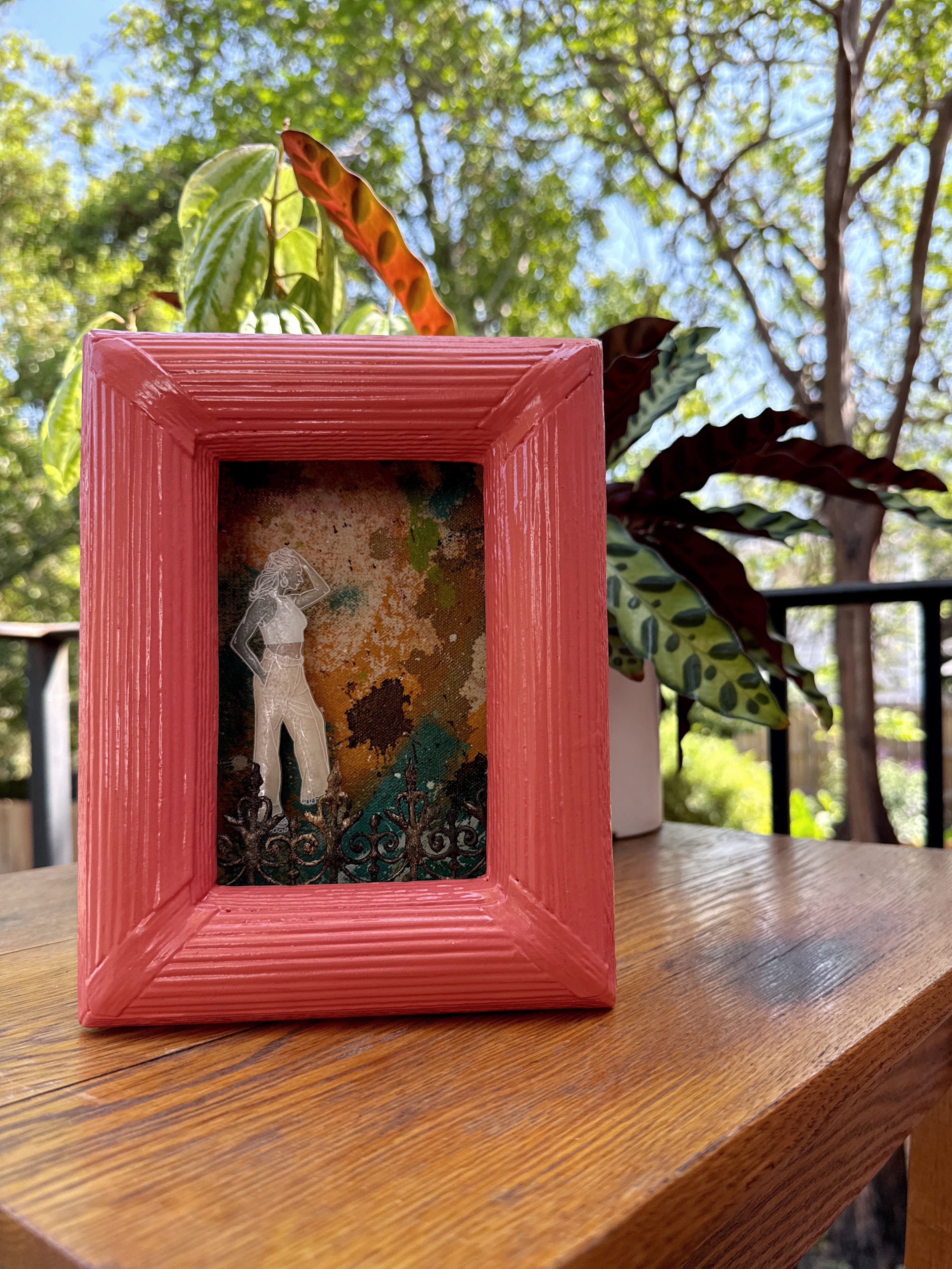 Small framed artwork on a wooden table with Southern plants in the background