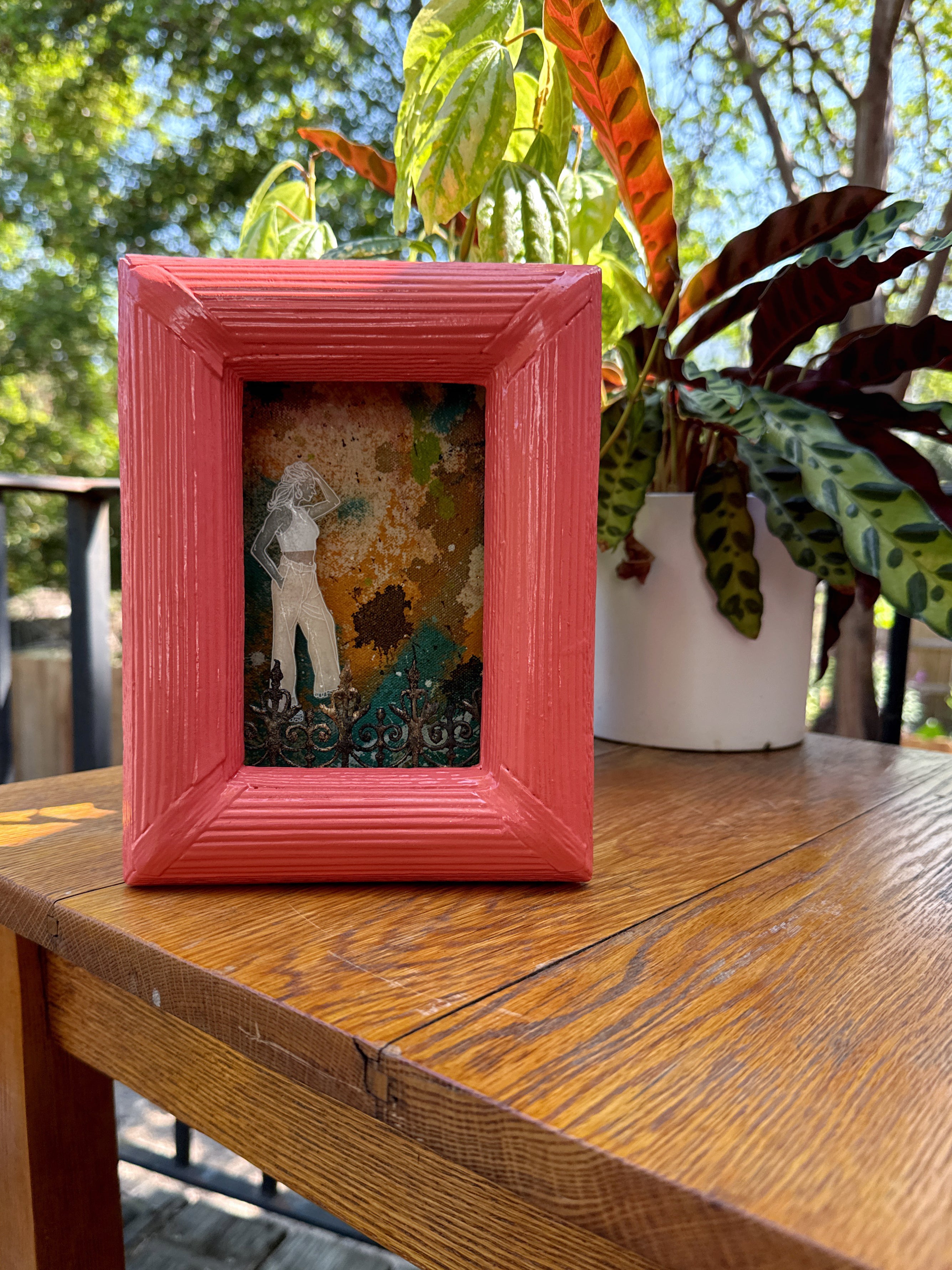 Framed artwork with a pink border on a wooden table outdoors in New Orleans