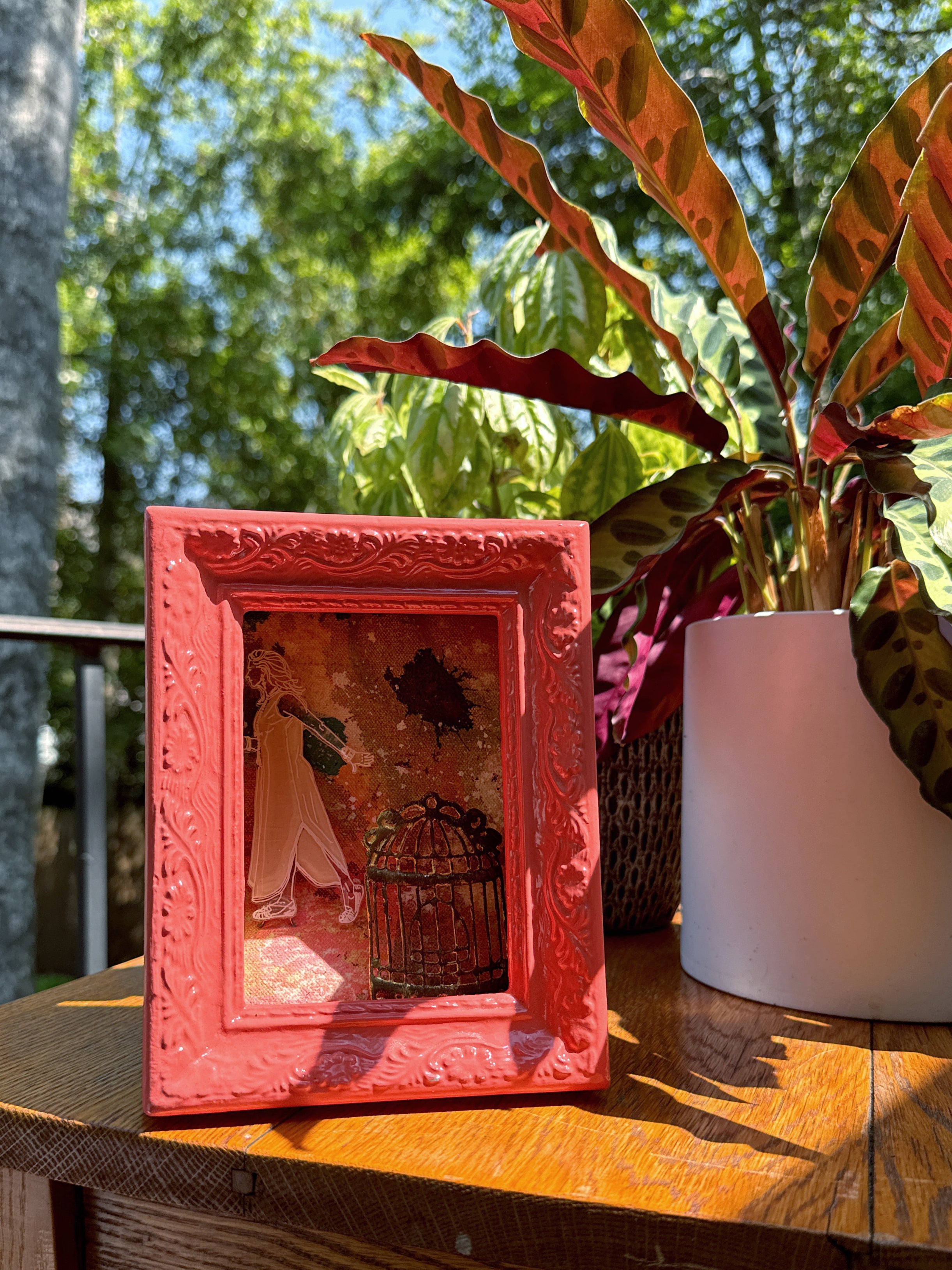 Pink decorative frame with a small artwork on a wooden surface outdoors