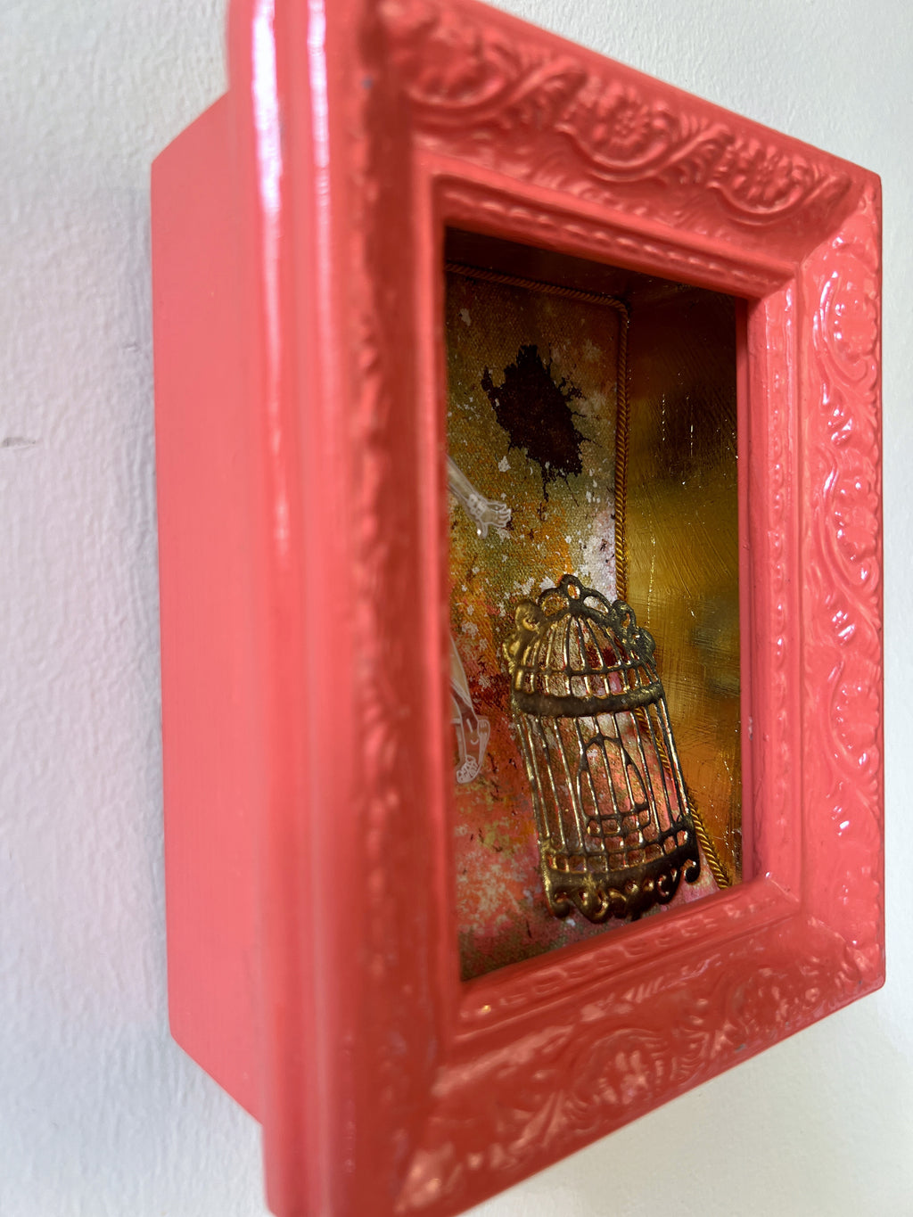 Decorative shadow box with a red frame containing a small birdcage and decorative elements on a white background